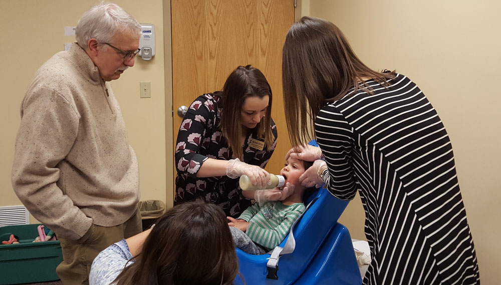 a photo of Dr. Ruscello working with a young girl on bottle feeding