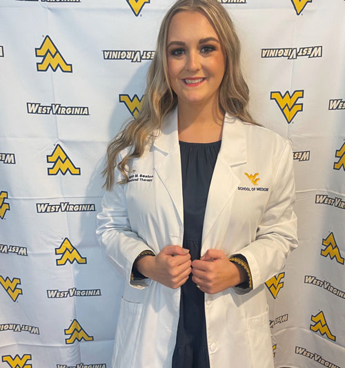 a photo of Meagan in her lab coat in front of a WVU banner