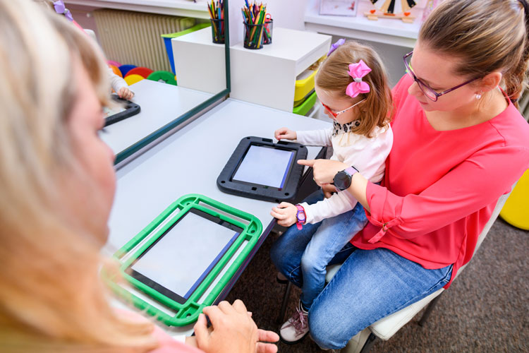 Child using a tablet-based communication device with assistance from a caregiver